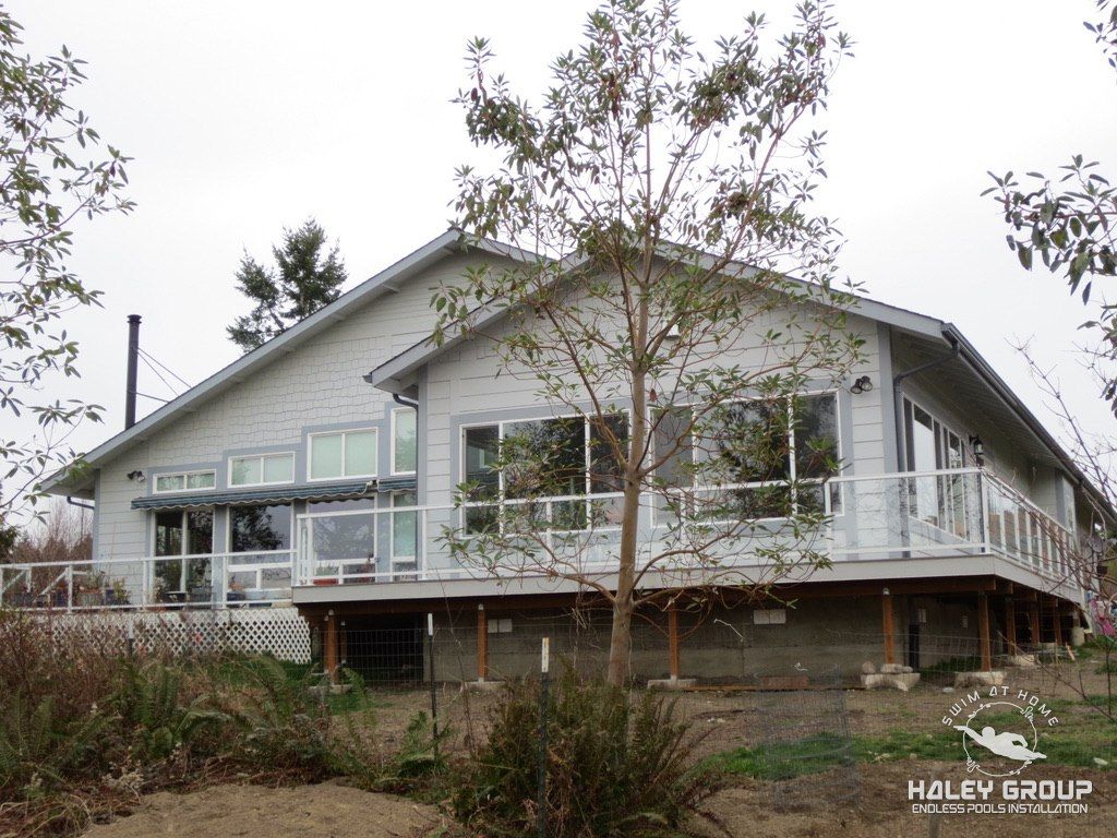 Exterior: gray home with the new sunroom wing over a raised deck with glass railing