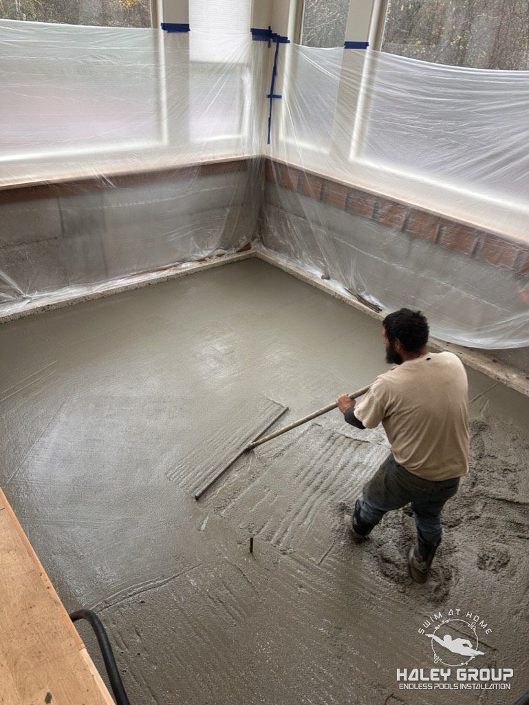 Crew member screeding the fresh concrete pad, with the windows wrapped in plastic