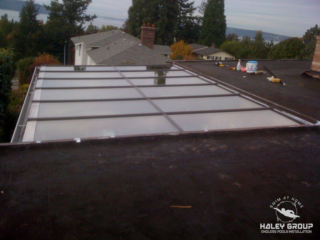 Large flat glass skylight roof set into a flat roof, with water views beyond