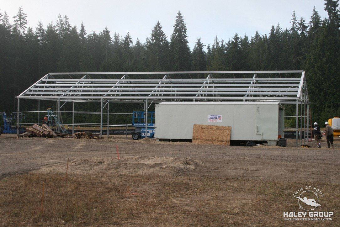 Steel gable greenhouse frame going up against a forest backdrop