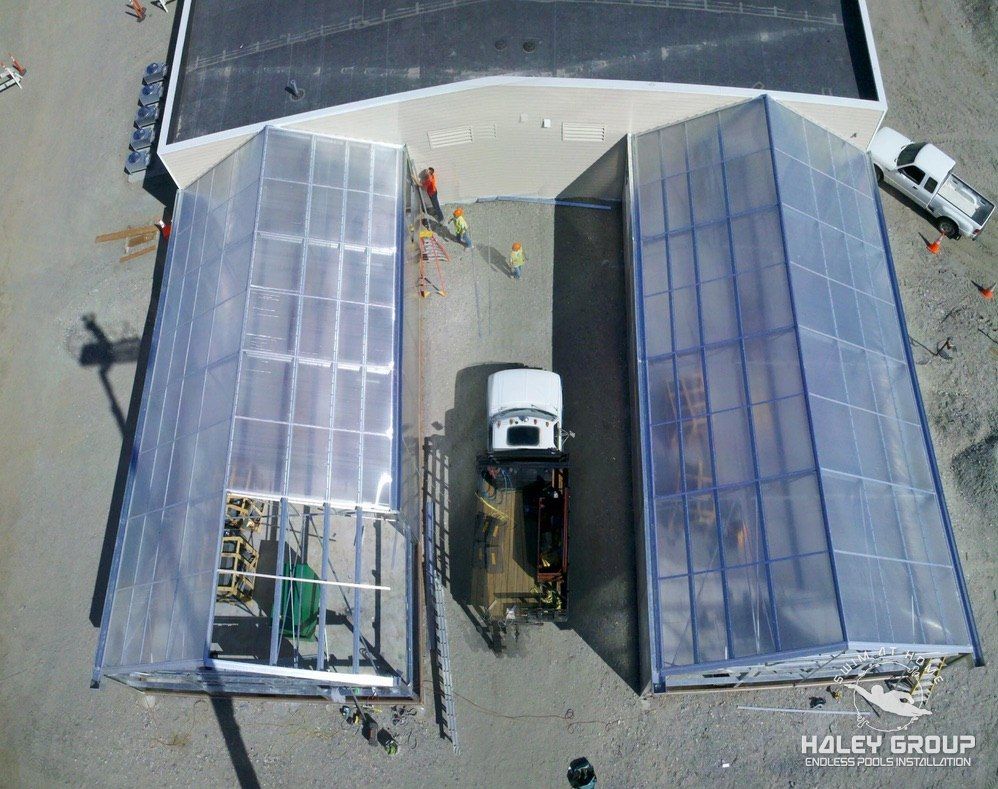 Aerial view of twin lean-to greenhouses going up against a building, with crew at work