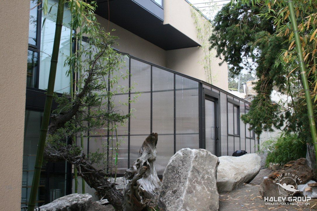 Translucent multiwall glazed enclosure with dark aluminum framing beside a modern home in West Seattle, WA, set in a bamboo and boulder garden