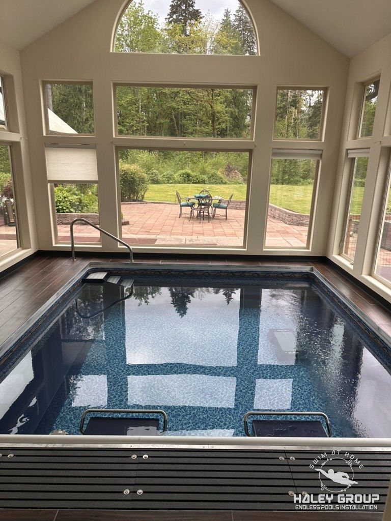 Indoor Endless Pool with stainless handrail and composite deck, under a wall of arched windows looking onto a garden patio, private residence in Maple Valley, WA